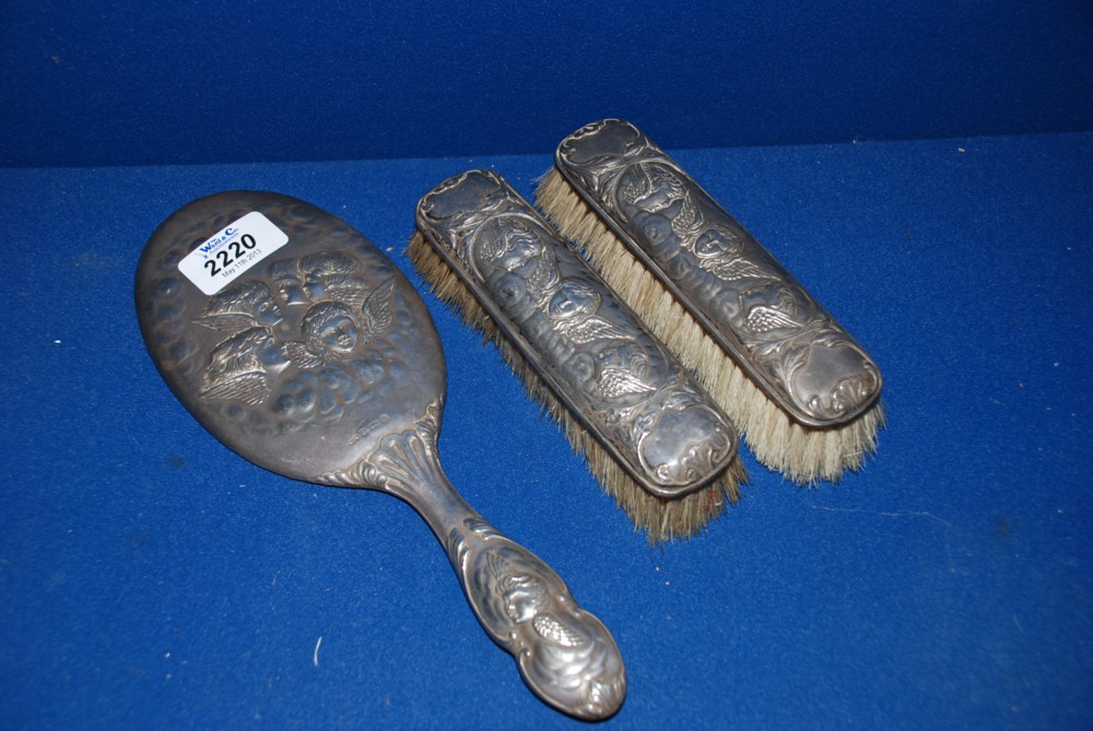 A Silver backed hand Mirror and two Brushes decorated with cherub heads