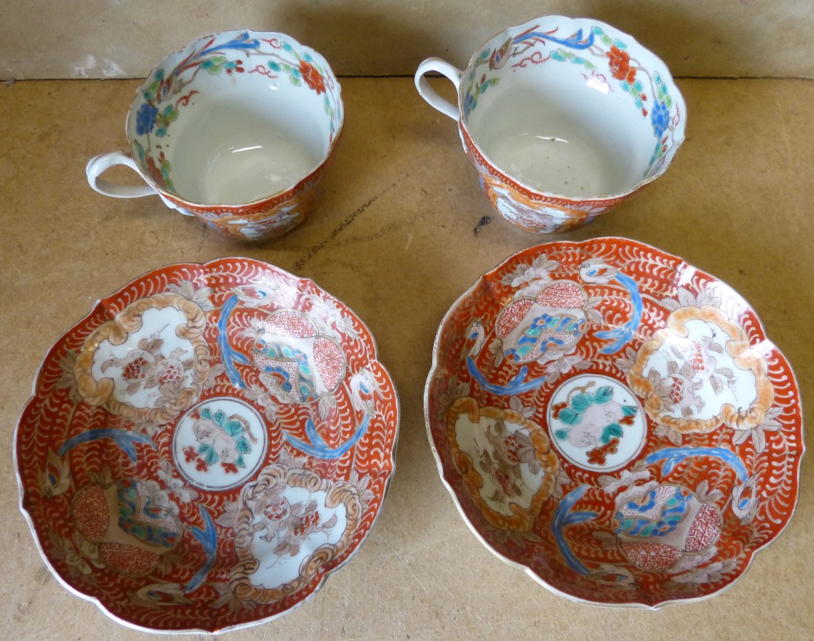 A Pair Oriental Cups and Saucers on red ground with multicoloured bird, floral, leaf and scroll