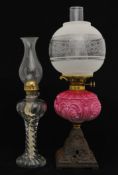 A Victorian oil lamp with pink glass reservoir and cast iron base together with another glass oil