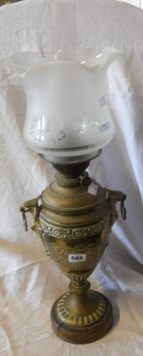 A brass urn shaped table lamp with griffin mounts, chimney and milk glass shade