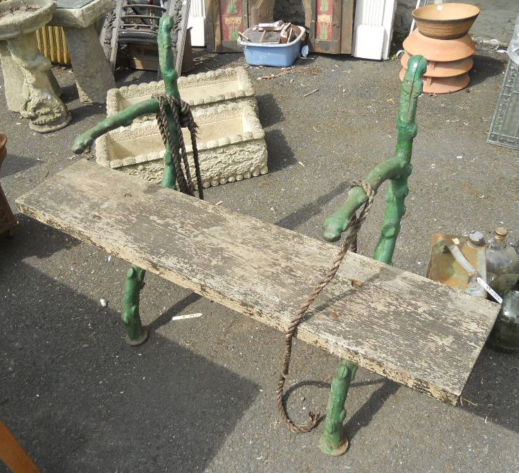 An antique green painted wrought iron garden bench with plank seat