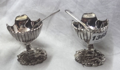 A pair of silver plated shell pattern salts with spoons and dolphin supports