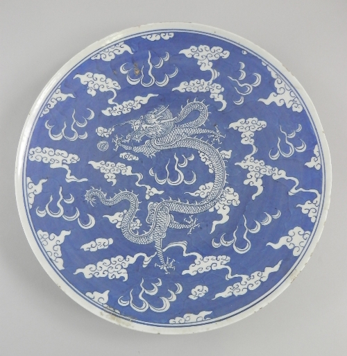 A Chinese blue and white dragon plate, central dragon surrounded by stylised coulds over blue ground