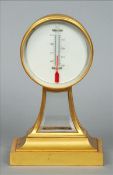 A gilt bronzed cased desk top thermometer The dial housed in a roundel above a bevelled glass
