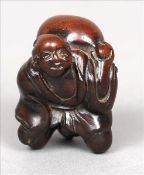 A late 19th/early 20th century Japanese carved hardwood netsuke Formed as a cloaked figure holding a