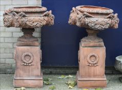 A pair of terracotta garden urns Each decorated with four rams heads between scrolling foliage,