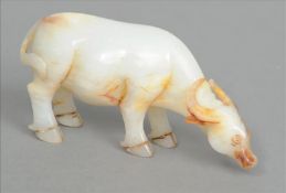 A Chinese carved white and russet jade water buffalo Naturalistically modelled grazing. 12 cms long.