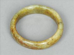 A Chinese carved green and russet jade bangle Of plain circular section with incised scrolling