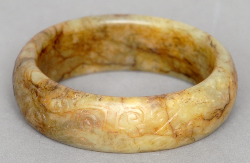 A Chinese carved russet jade bangle The exterior decorated with stylised scrolls. 9 cms diameter.