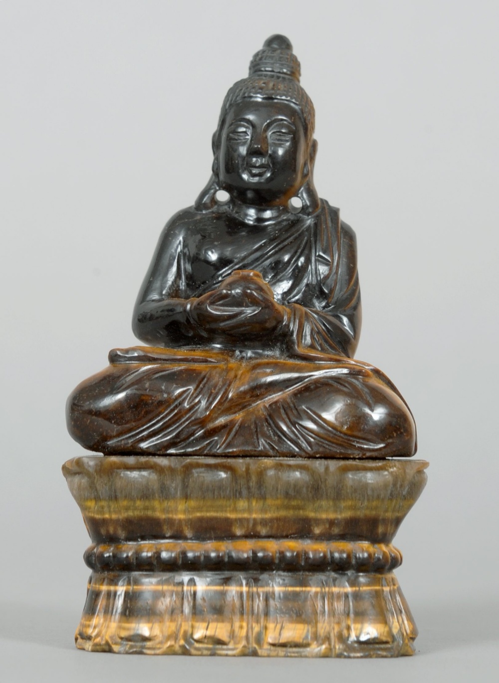 A Chinese carved “tiger’s eye” carved figure of Buddha Modelled holding a gourd and seated in the