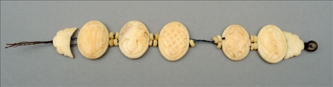 A carved bone bracelet Strung with five variously carved oval panels. 19.5 cms long. Some wear,