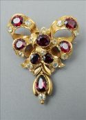 A Victorian unmarked gold, garnet and citrine brooch Of bow tied ribbon form with a central drop.