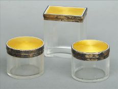 Three Art Deco enamel decorated silver lidded glass jars Two of circular form, one rectangular, each