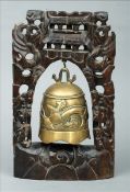 An Oriental bronze temple bell and a white metal inlaid carved hardwood stand 37 cms high. Some