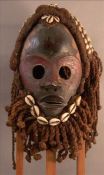 A carved African tribal mask With applied cowrie and other shells and rope twist hair and beard. The