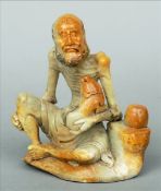 A Chinese soapstone carving Modelled as an emaciated bearded man holding a shi-shi. 16 cms high.