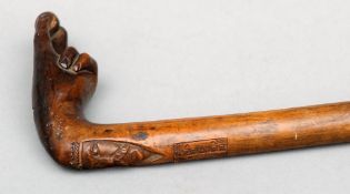 A Greek olive wood walking stick The handle formed as a hand holding an olive above a carved face