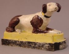 An early 19th century English pottery dog Modelled recumbent on stepped plinth base. 10 cms high.