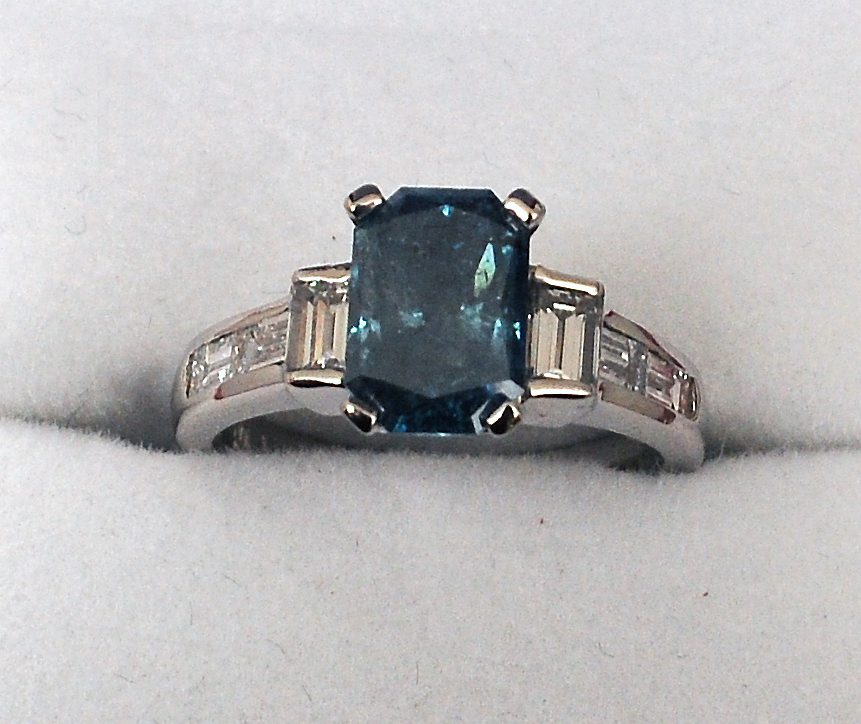 An Art Deco style blue diamond and platinum ring The central cushion cut stone approximately 2