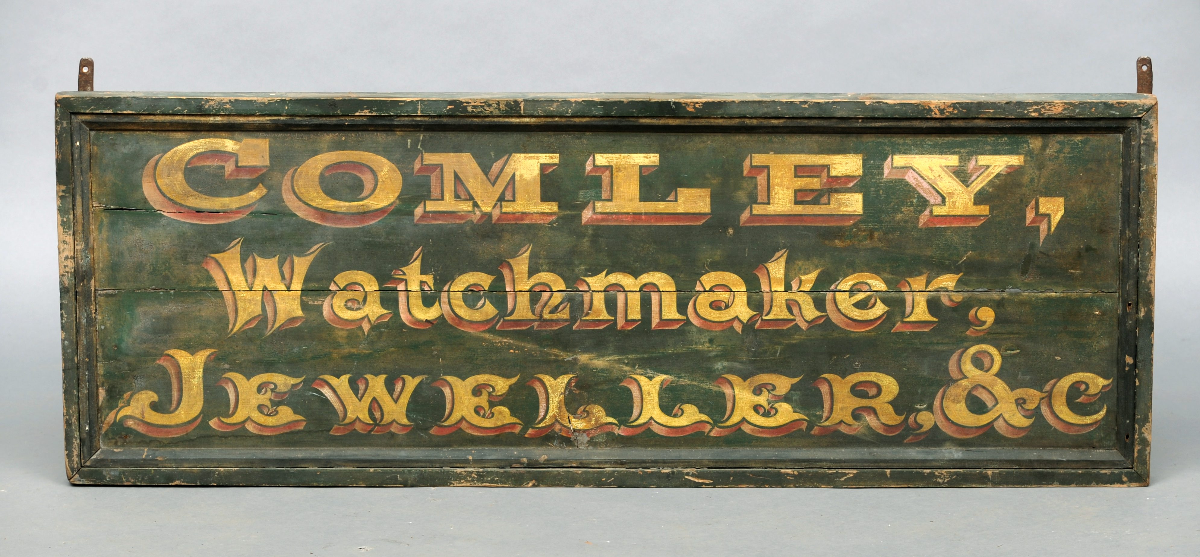 A 19th century painted wood watchmaker’s sign Inscribed Comley, Watchmaker, Jeweller & C, on a green