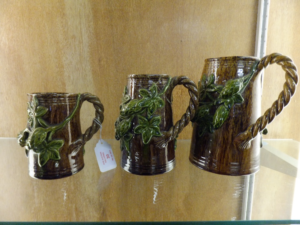 A set of three graduating Rye Pottery brown glazed jugs having applied hop decoration to the body