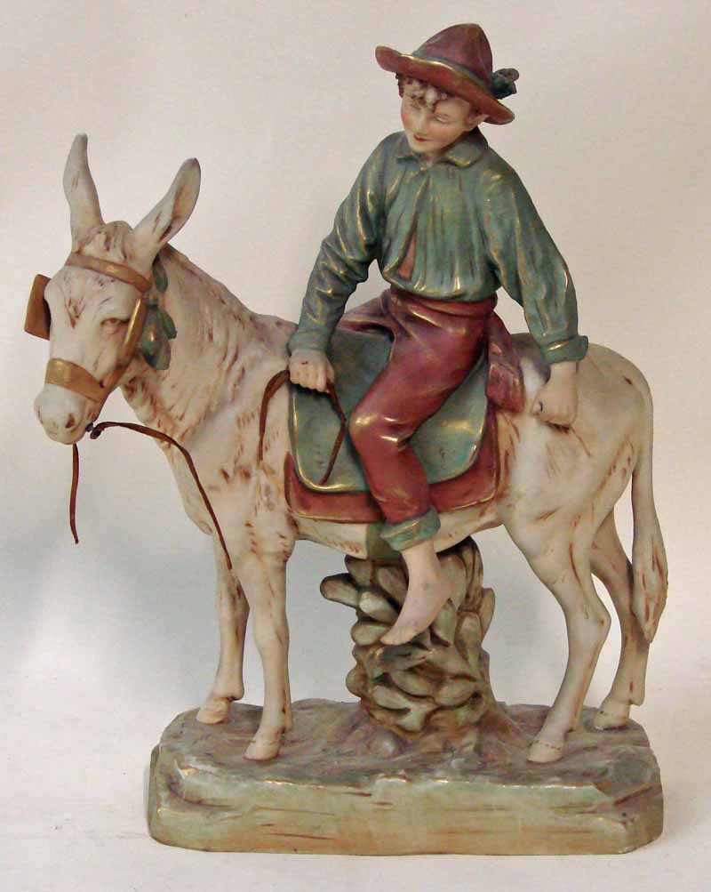 A Royal Dux figural model of a boy riding a donkey, raised on naturalistic base, decorated in