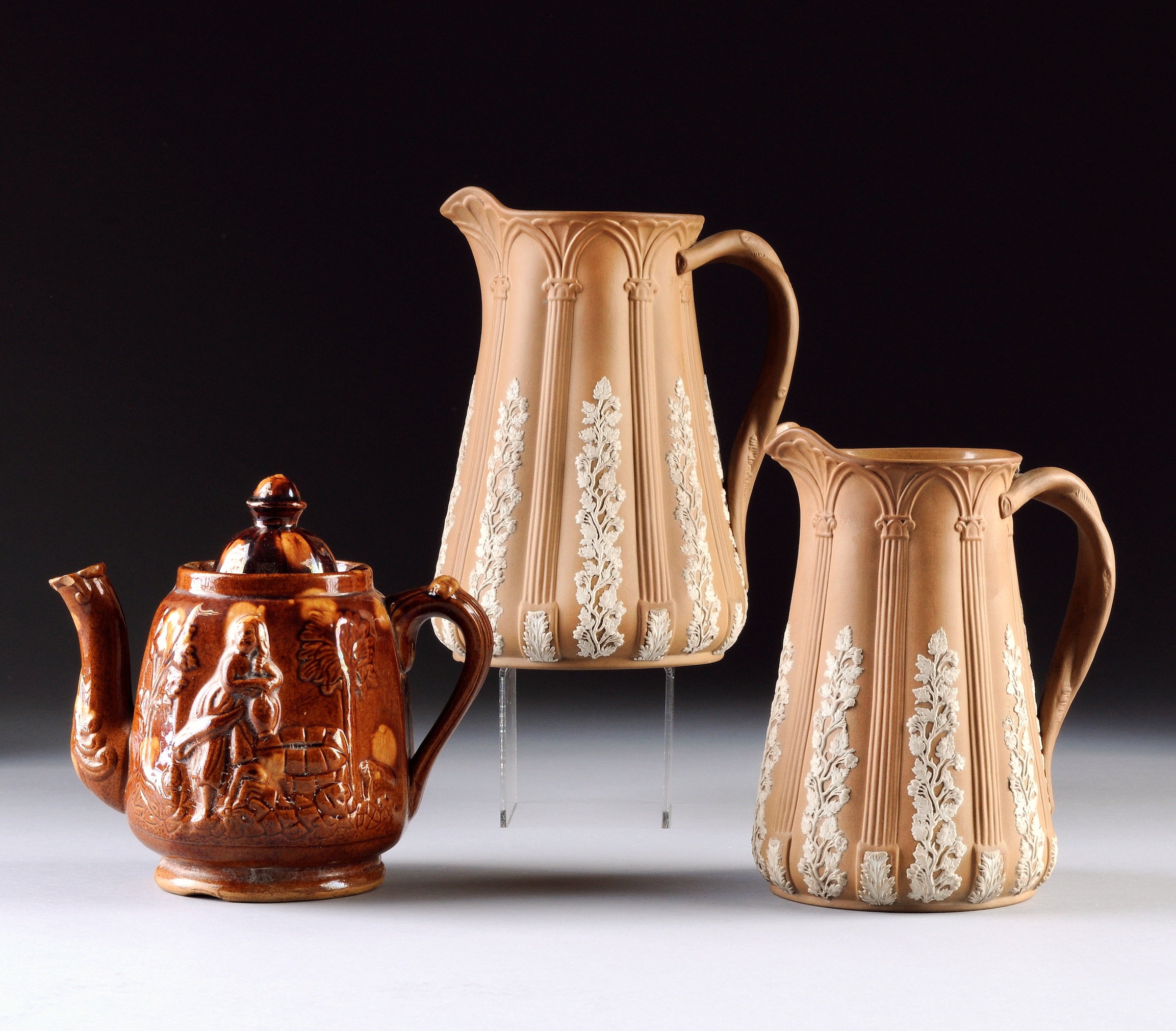 TWO ENGLISH WHITE ON BROWN BASALT WARE PITCHERS AND A BROWN SLIP GLAZED EARTHENWARE TEAPOT, 19TH