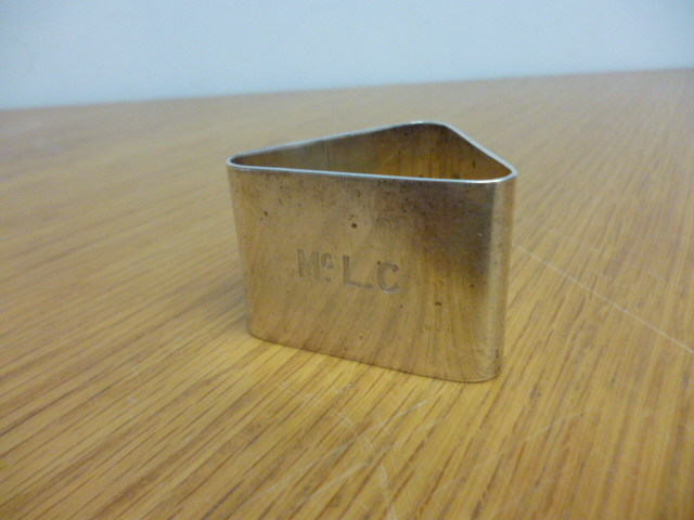 An early 20th century triangular silver napkin ring with the initials Mc.L.C to the front (1) NO