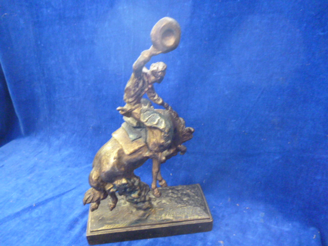 A plaster filled bronzed figure of a cowboy riding a bucking horse signed Paul Herzel to base NO