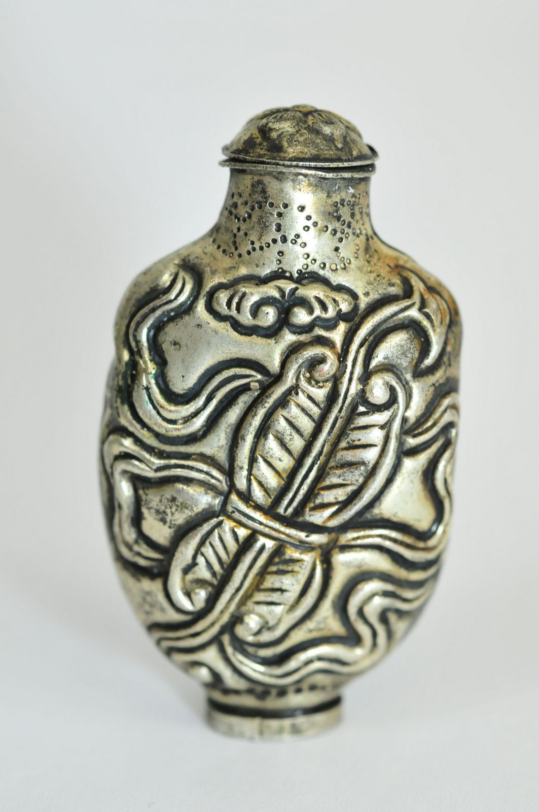 An oriental style white metal snuff bottle having foliate design.