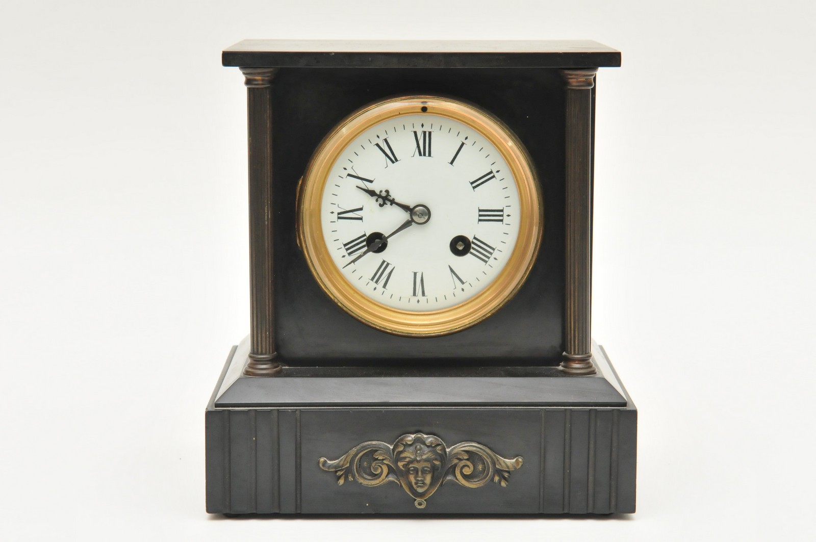 A black slate mantle clock having Roman numerals, flanked by pillars and having cherub decoration.