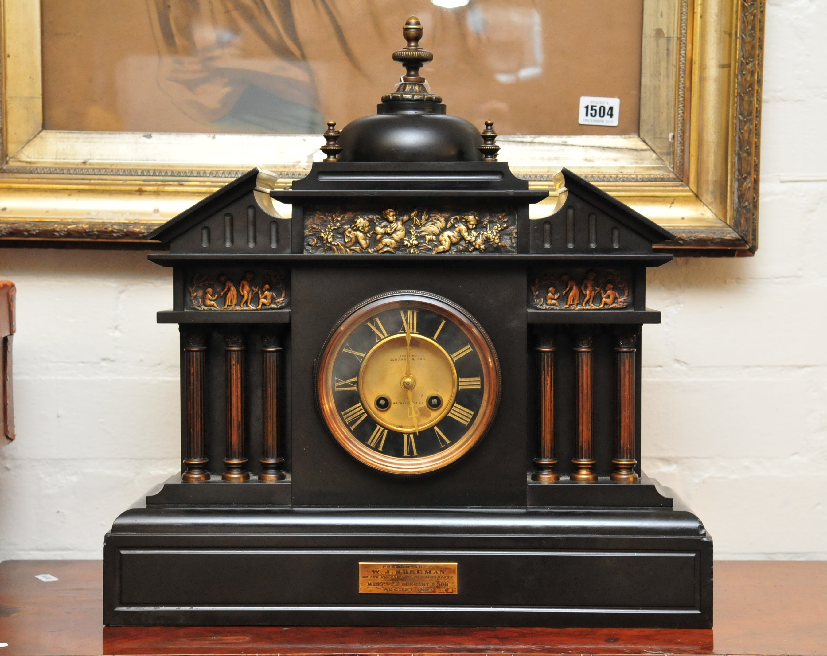 A large black slate mantle clock of classical style flanked with classical columns having split