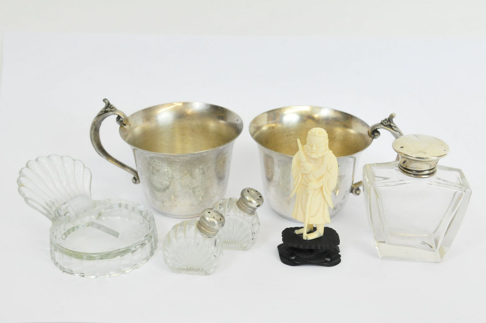 A small ivory carving, three silver topped glass bottles and two plated cups