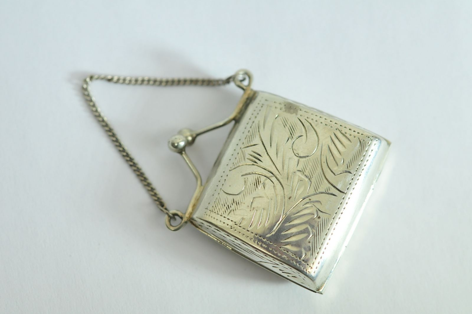 A small silver hallmarked snuff box in the shape of a ladies handbag with embossed design.
