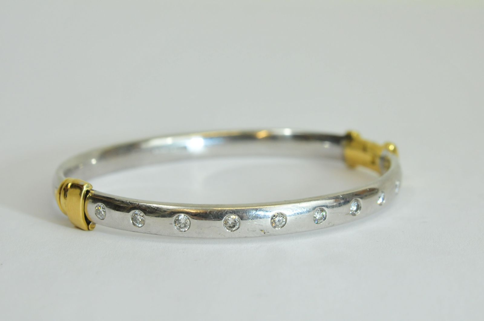 A ladies 18ct white gold bangle having yellow gold hinge and clasp, flush set with ten brilliant cut