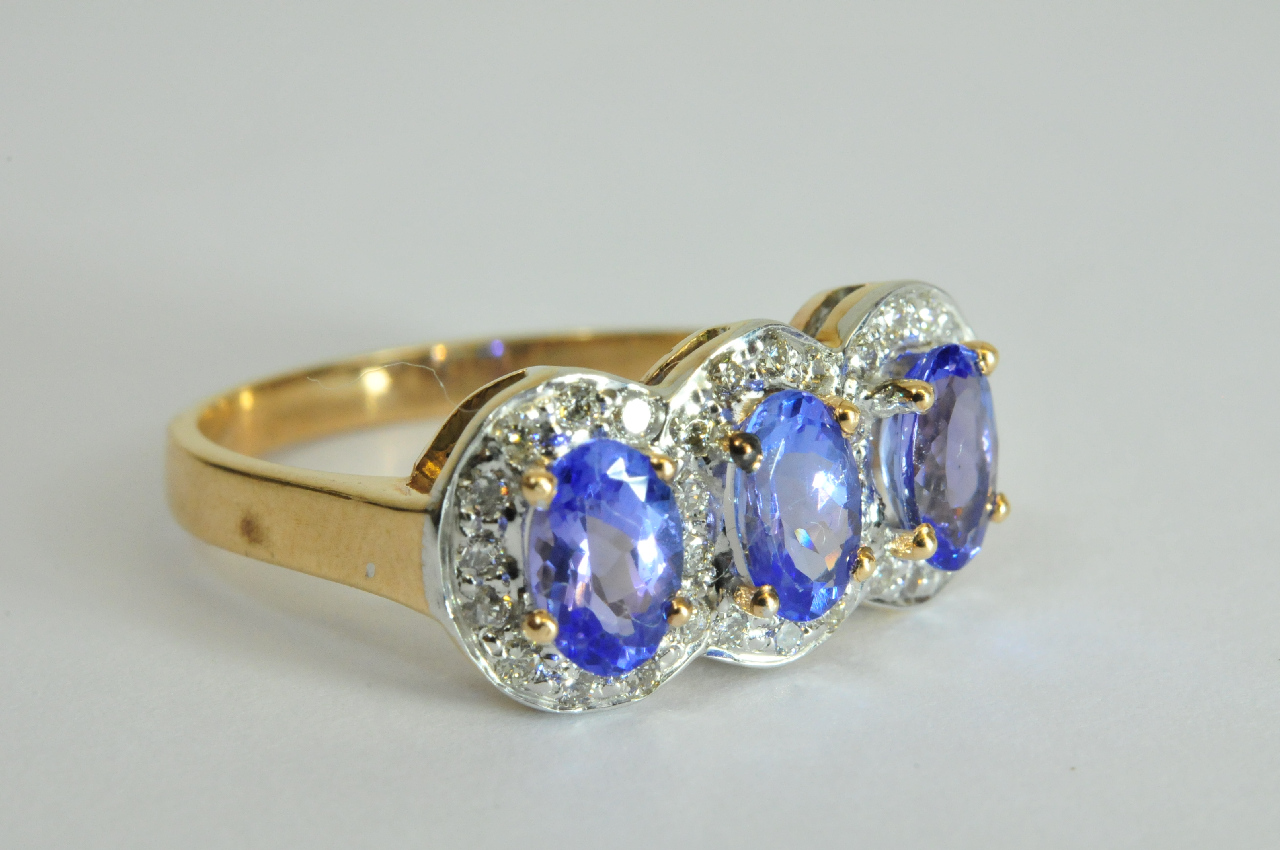 A ladies 9ct gold ring set with three oval cut tanzanite, each with diamond surround