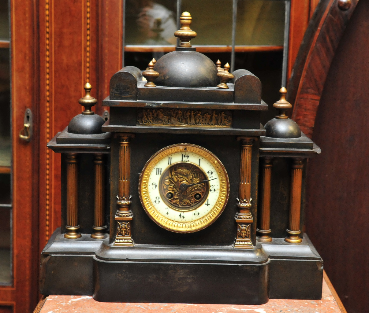 A black slate mantle clock flanked by classical columns, having brass finials to top and metal