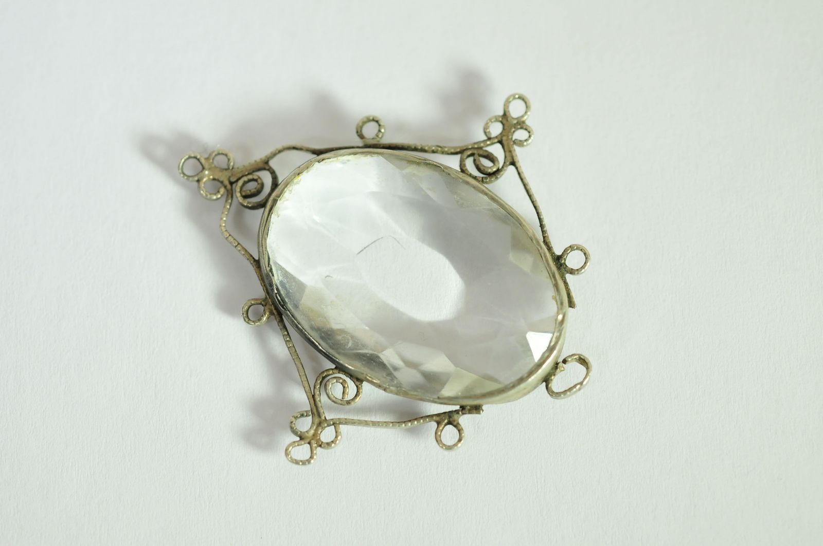 A glass pendant having white metal filigree framework.