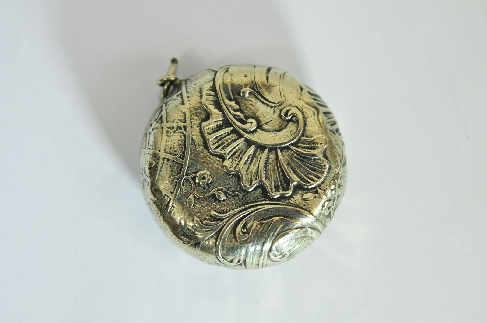 An embossed white metal round snuff box with hinged lid opening to a mirror.