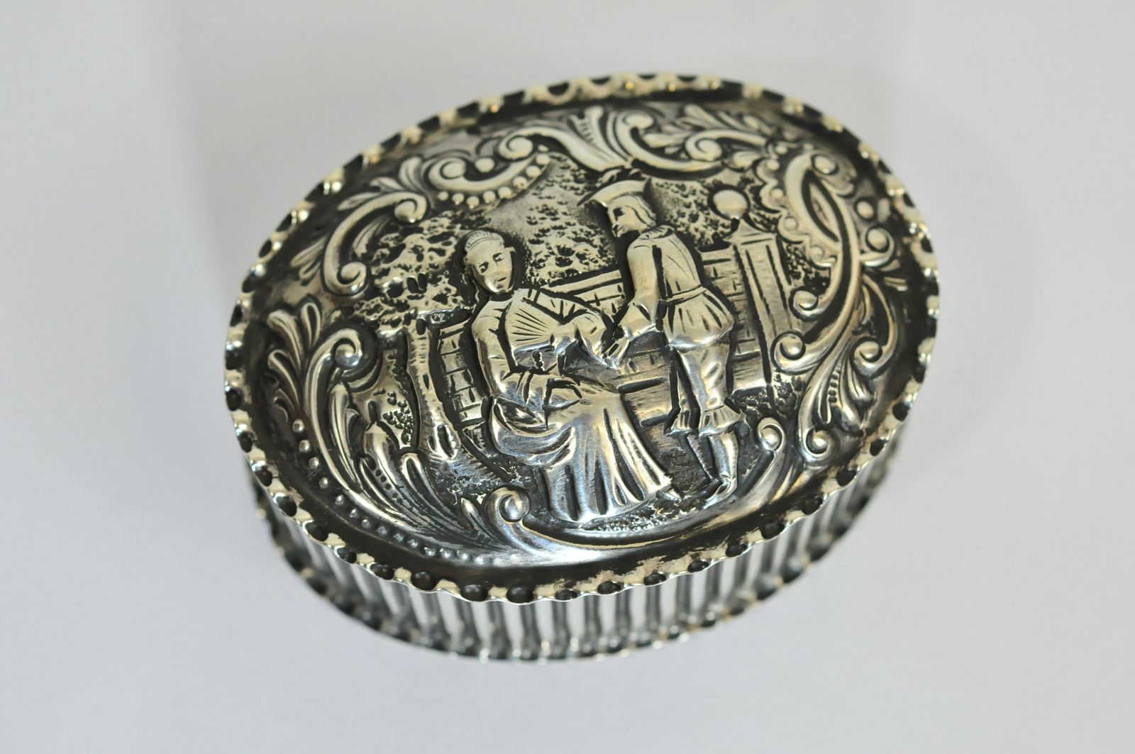 An embossed oval snuff box depicting a lady sitting on a park bench with a standing gentleman,