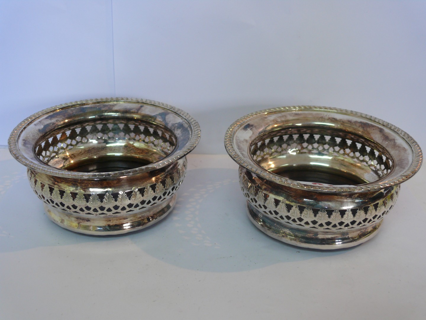 A pair of silver circular pierced wine bottle stands, having gadrooned rims and turned wooden bases,