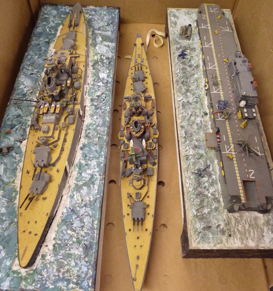 Three constructed painted plastic models of warships, two mounted on naturalistic "sea" base