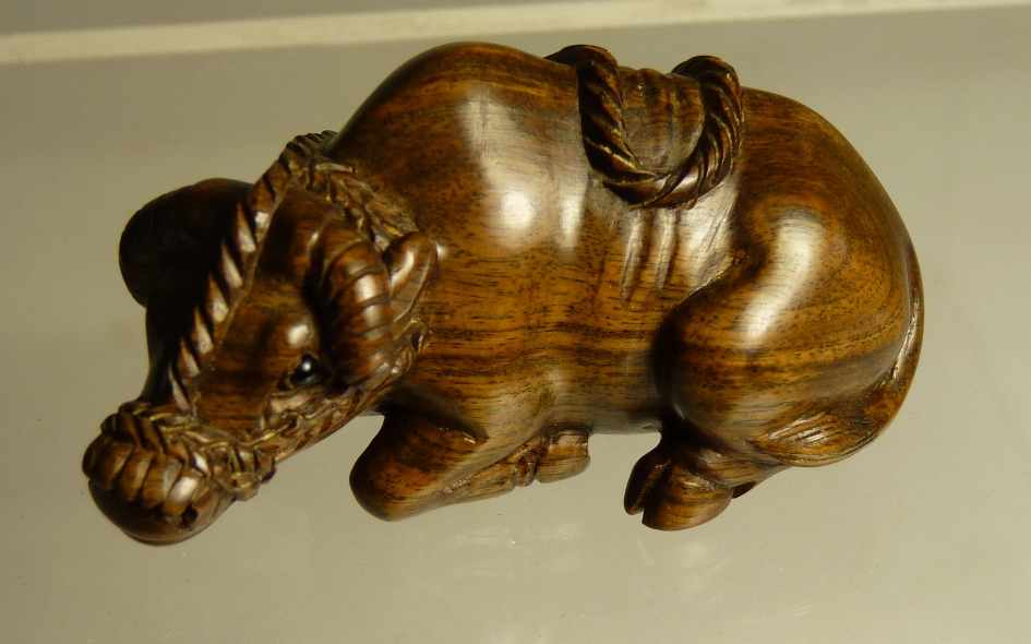 A Japanese carved wood netsuke of a recumbent buffalo wearing rope halter, inset character mark