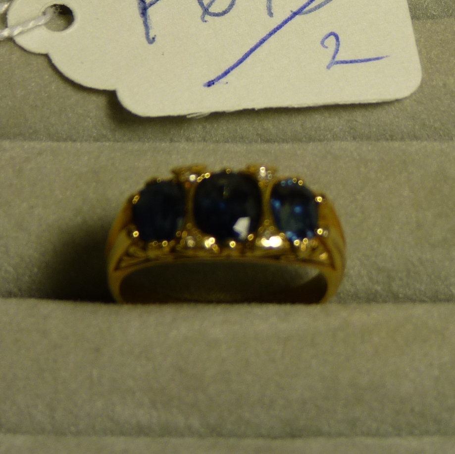 An 18ct gold three stone sapphire ring with small diamonds between the stones and in scroll setting
