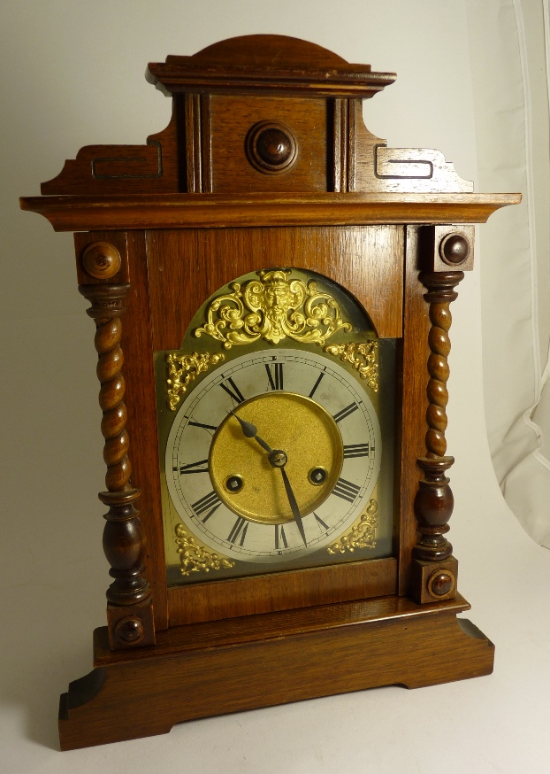 A late 19th Century mantel clock in stained wood architectural case having arched gilt dial with