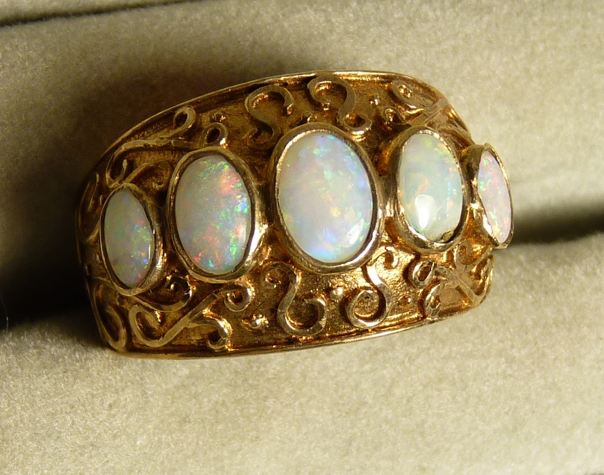 A wide 9ct gold ring set with five oval graduated opals, the band also with wirework decoration, 5.
