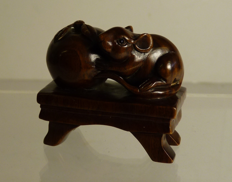 A Japanese carved wood netsuke of a rat holding an apple on a rectangular stool, 20th Century