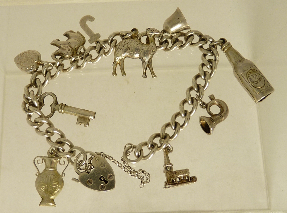 A silver charm bracelet with attached silver charms including a camel, a bell, elephant, vase,