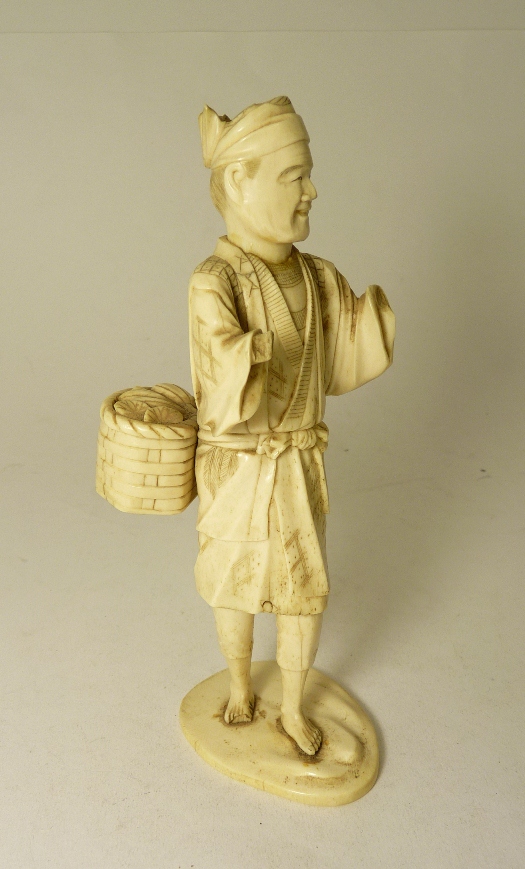 A Japanese carved ivory okimono of a man with a basket of fruit, 19.5cm approx (lacks part of both