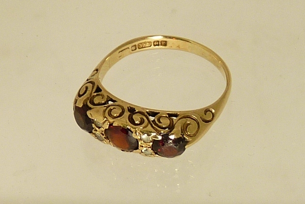 A 9ct gold dress ring, set with three circular faceted garnet coloured stones, spaced wtih small